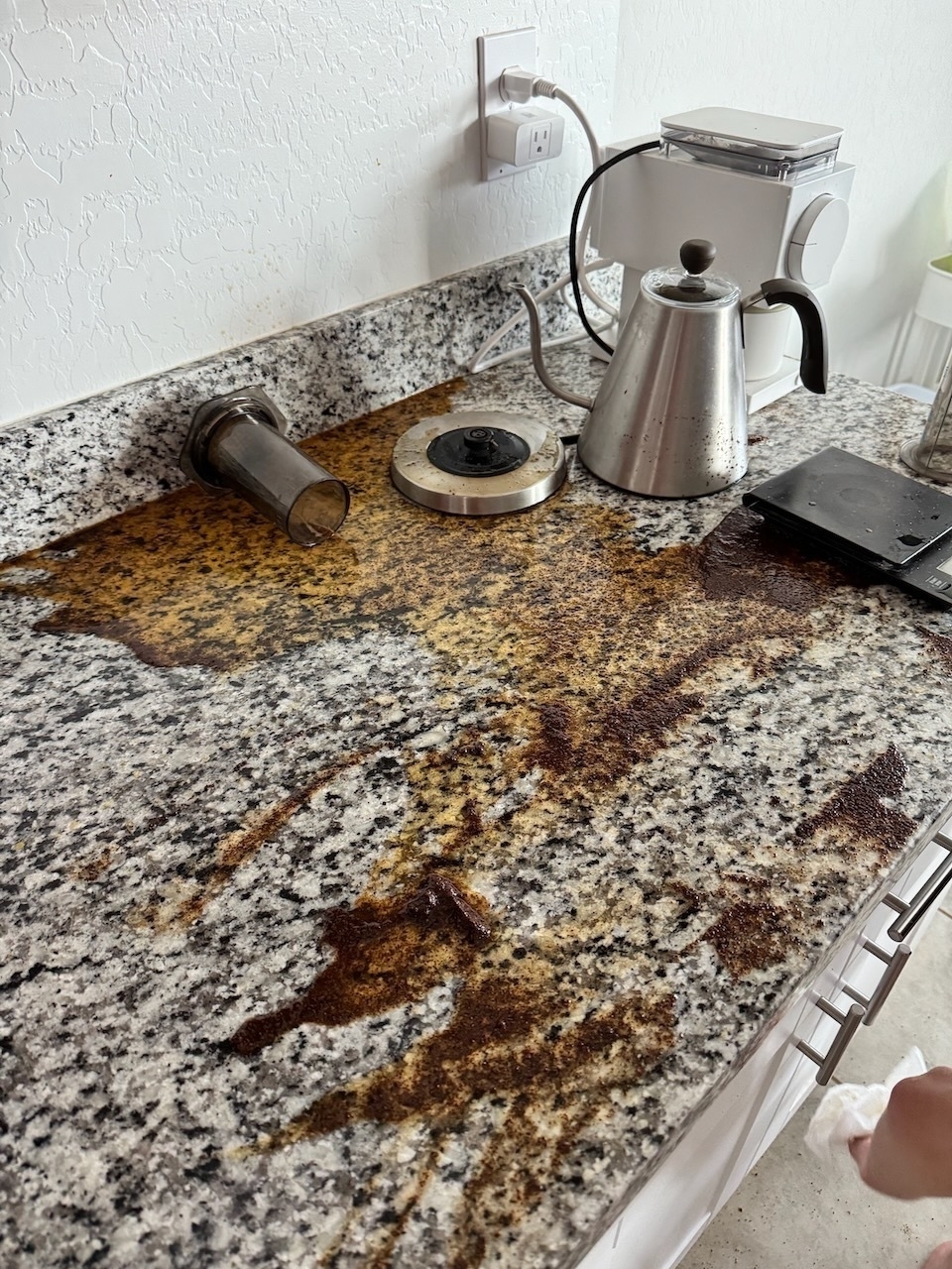 Strewn coffee equipment next to wet grounds and coffee on countertop